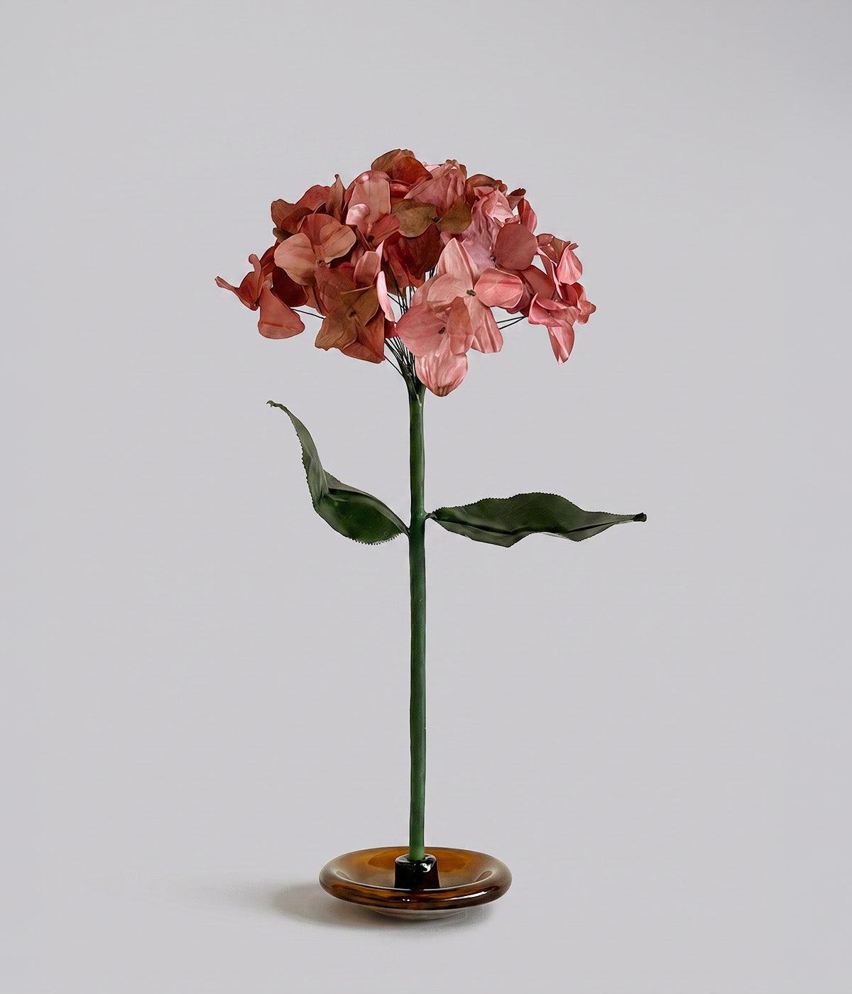 Autumn paper hydrangea with rose and russet florets, green leaves, and a mouth-blown glass stand.
