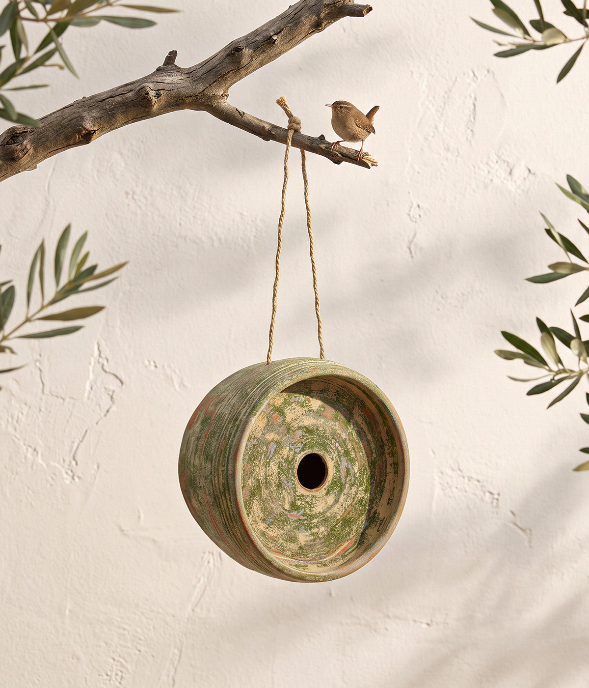 Garden Sage terracotta birdhouse hanging below a tree branch with a small bird perched above it