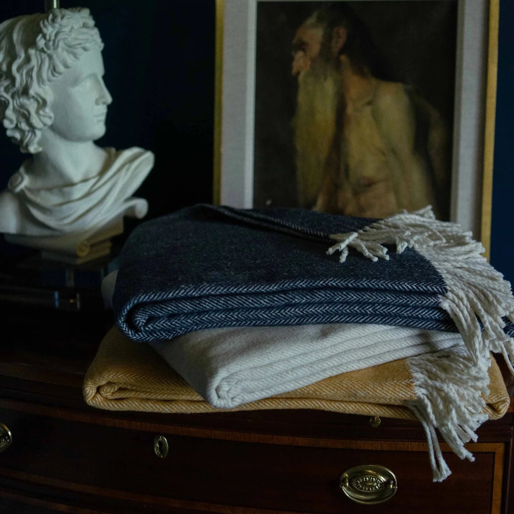 A moody picture with a stack of simple herringbone throws stacked on a table 