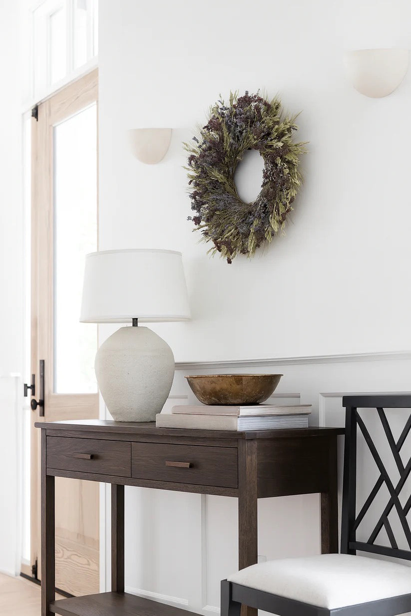 Beatrice wreath on wall above dark console with lamp and neutral decor