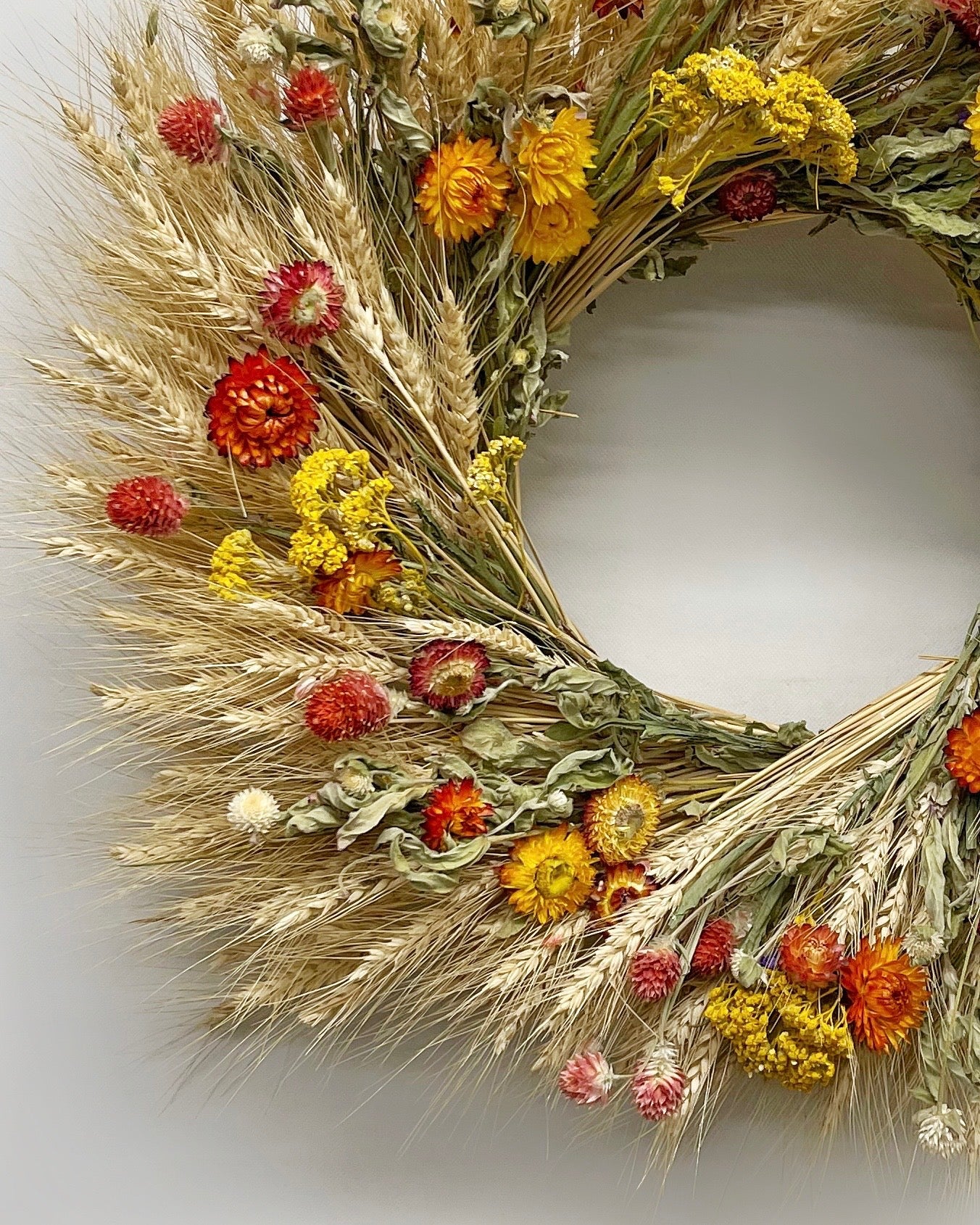 Close-up of Louisa wreath showing blonde wheat stalks, yellow yarrow, and coral globe amaranth