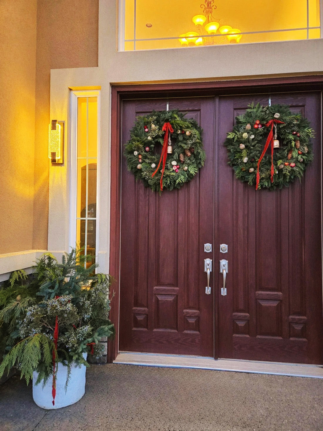 Two Juliette floral Christmas wreaths with red velvet ribbons and antique bells on double front doors
