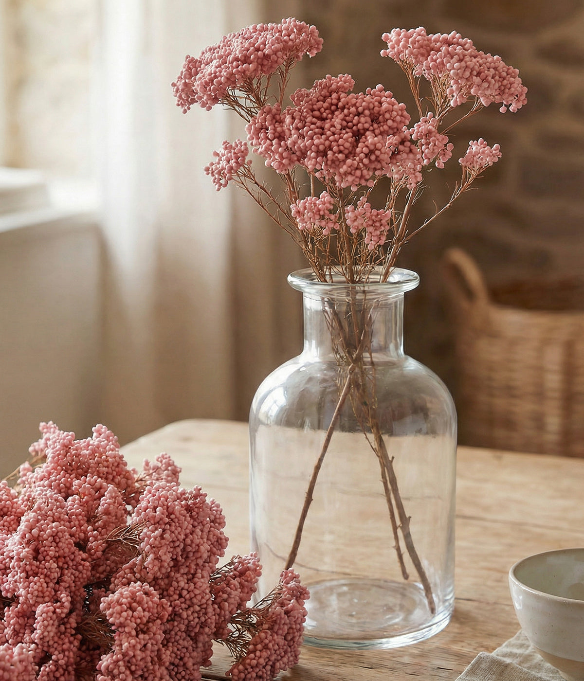 Preserved rice flower in pink arranged in a clear glass vase on a tabletop