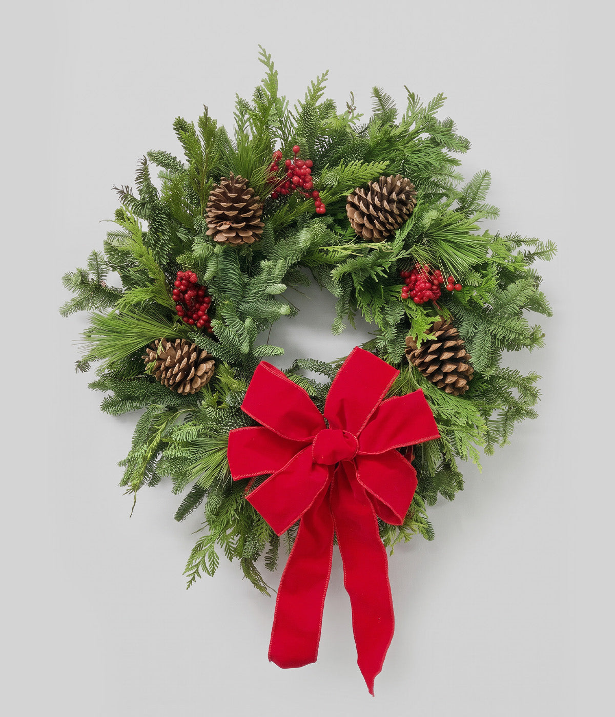 Ruby Christmas wreath with red bow, fresh greenery, red canella berries, and ponderosa pine cones
