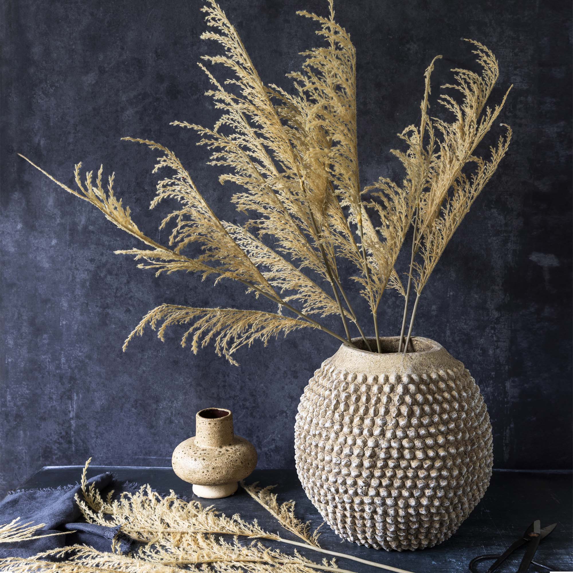 Artificial botanical grass stem styled in a ceramic vase on a shelf display