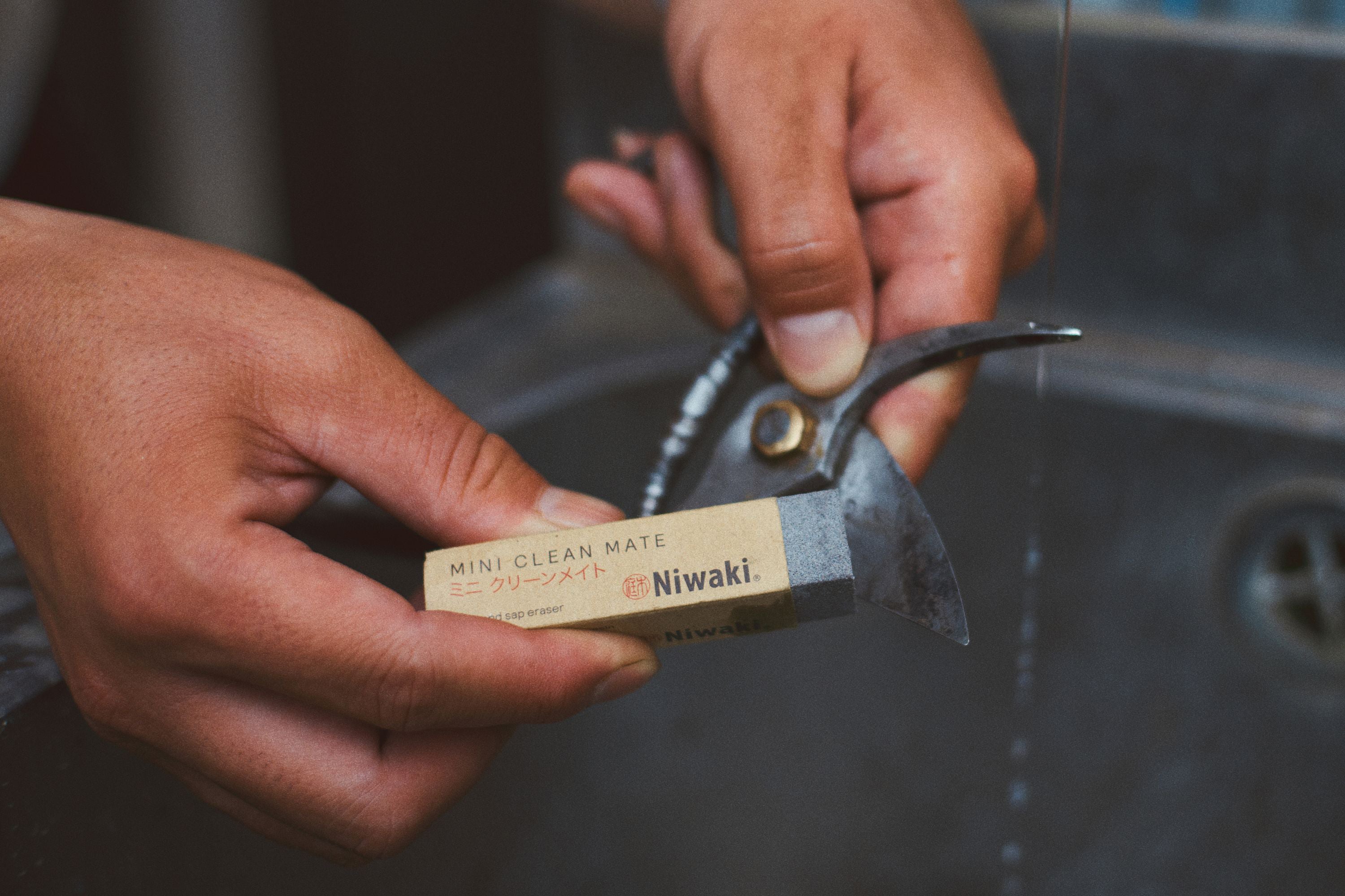 A pair of hands using a garden tool cleaner to remove sap and rust from pruning shears